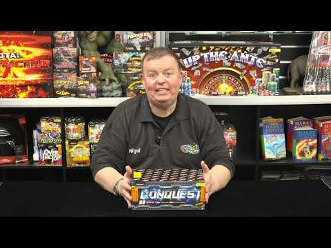 Presenter showcasing Conquest 90-shot fanned cake by Primed Pyrotechnics in a fireworks store, highlighting product features.