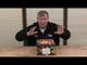 Presenter showcasing Legion 100-shot cake by Black Panther Fireworks, highlighting features and packaging design on a review table.
